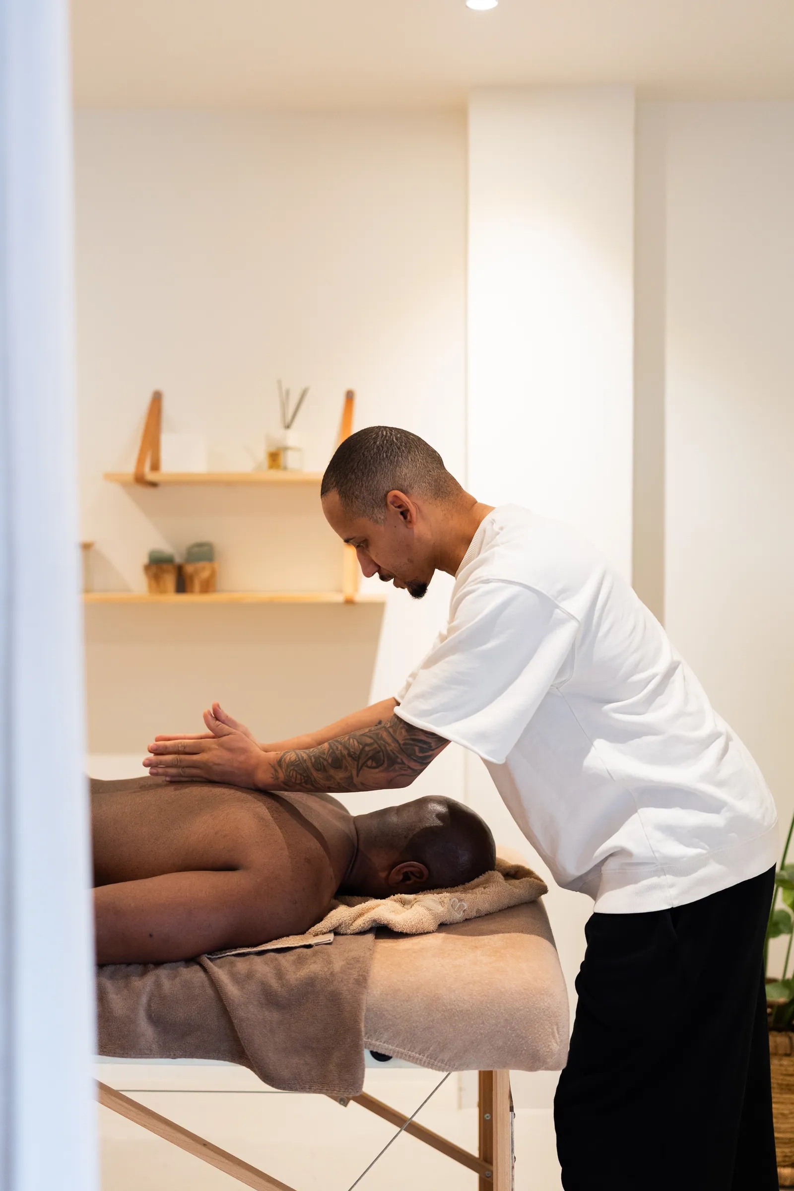 Sportmasseur masseert rug van cliënt op massagetafel in rustige witte ruimte.