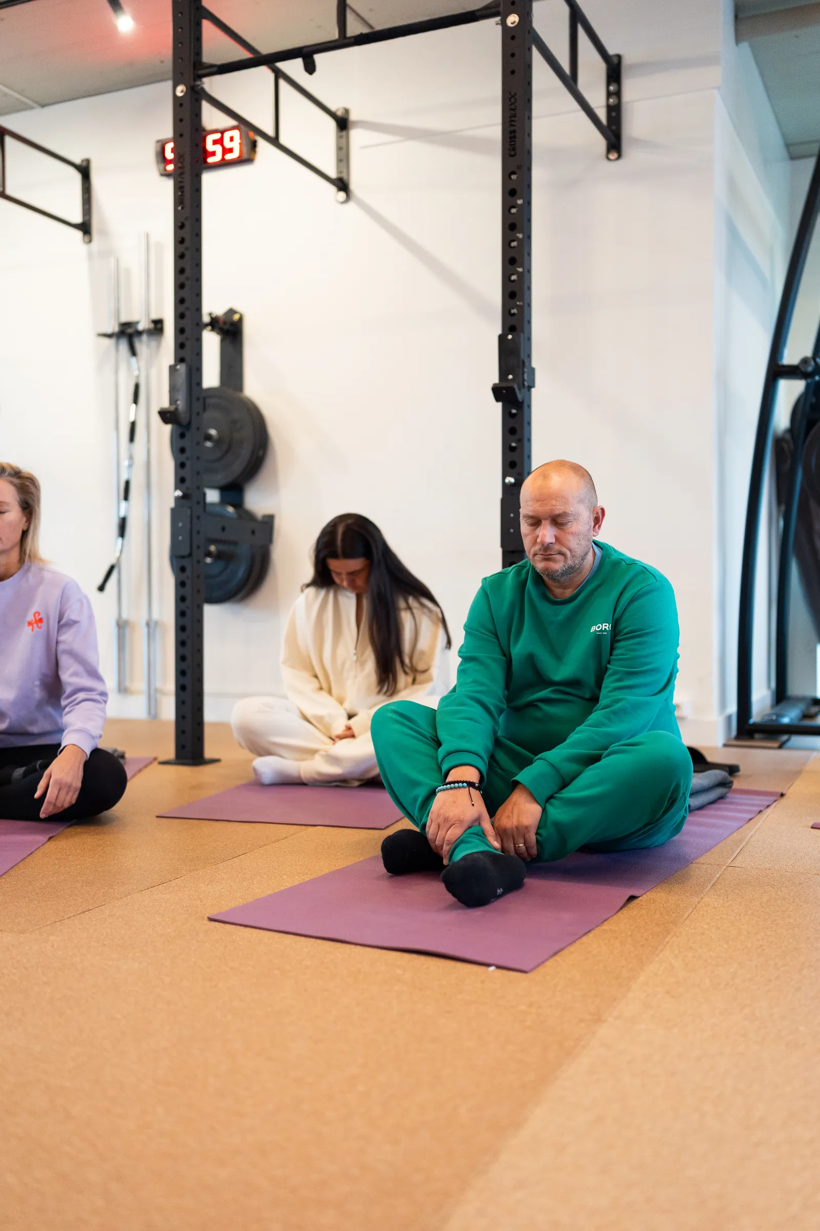 Man in groene trainingspak mediteert op mat tussen andere deelnemers.
