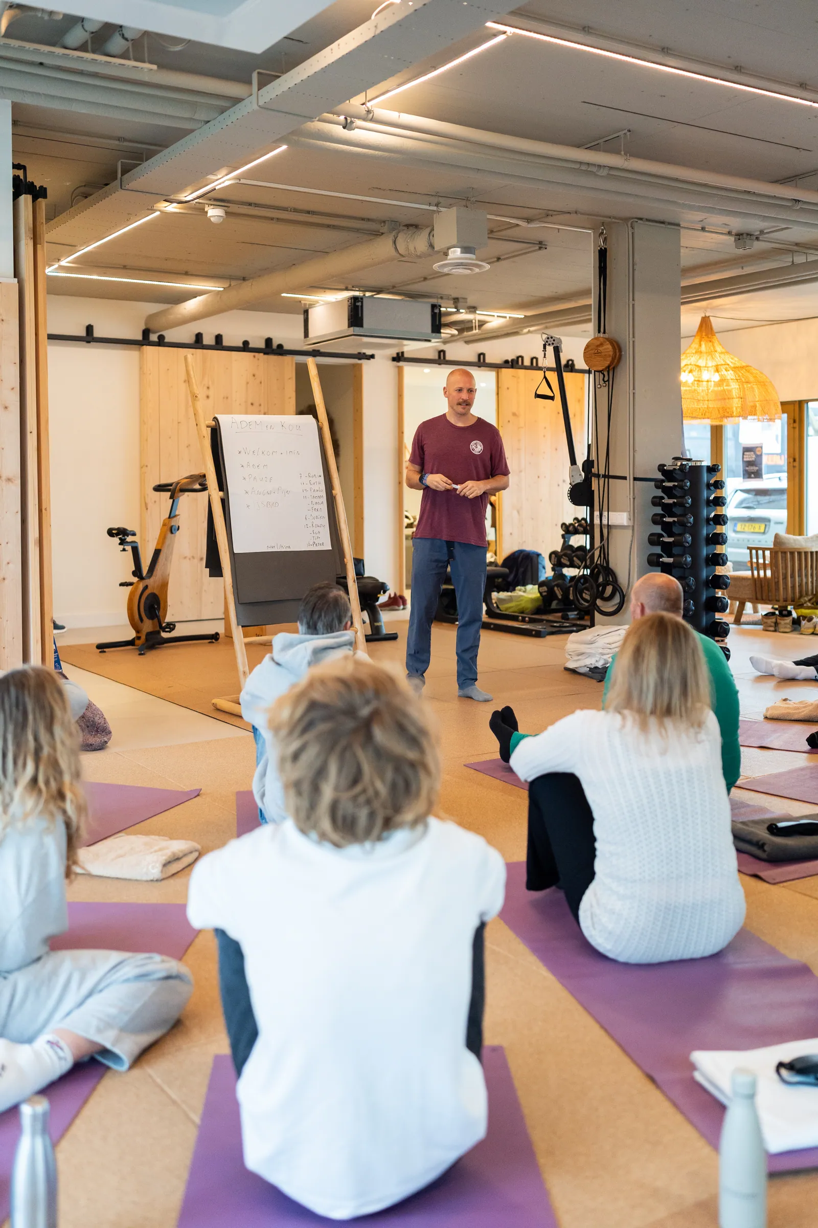 Coach bij whiteboard met groep op matten; sportschool op achtergrond.